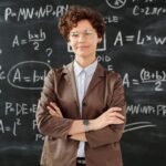 Confident female teacher standing with arms crossed in front of a detailed mathematical blackboard.