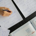 Close-up of a student solving mathematical equations with papers and textbook on a table.